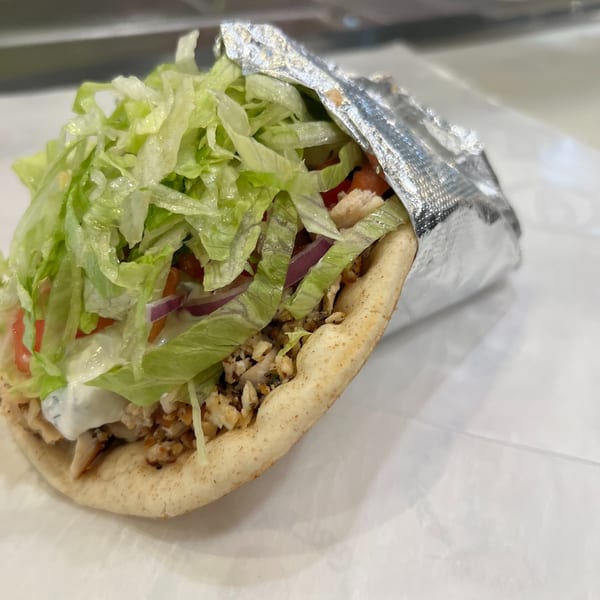 A Greek Lady chicken gyro with lettuce, red onion, tomatoes, and tzatziki sauce, wrapped in foil.