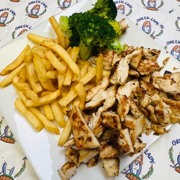 Grilled chicken pieces, golden french fries, and steamed broccoli on a white plate with a Greek Lady branded tablecloth.