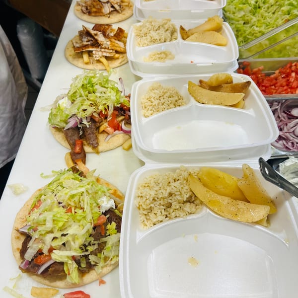 Greek gyros, chicken pita, rice, and potatoes in takeout containers on a white counter.