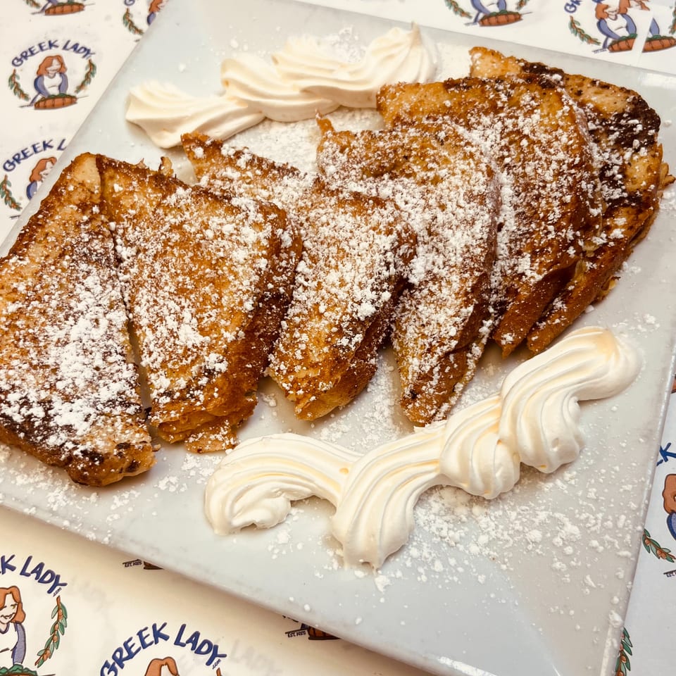 Golden French toast slices dusted with powdered sugar and garnished with whipped cream on a white plate.