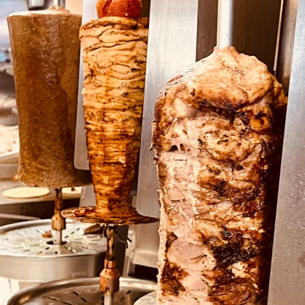 Three vertical rotisseries with different types of Greek meat, including gyros and doner.