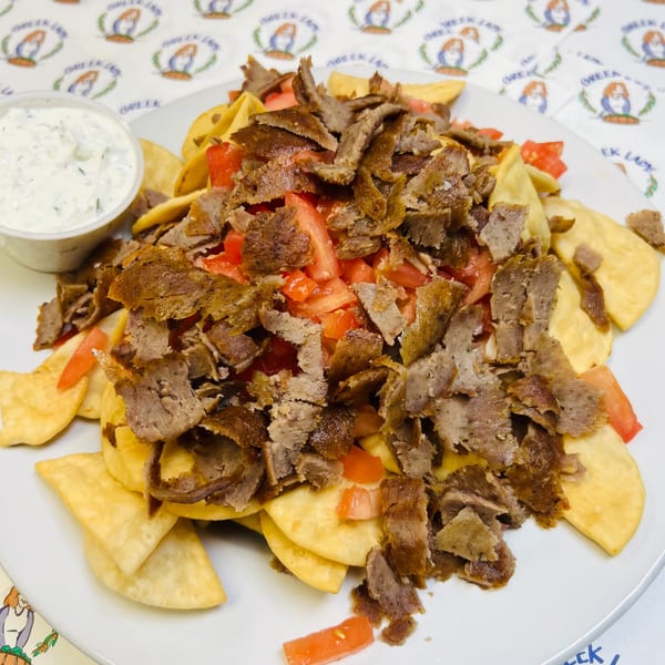 Greek nachos with gyro meat, diced tomatoes, and a side of tzatziki sauce on a white plate.