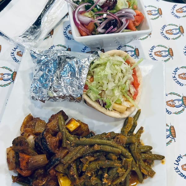 A Greek Lady meal with a gyro, side salad, and two vegetable dishes on a branded paper.