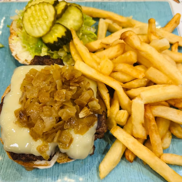 A Greek Lady burger with melted cheese, caramelized onions, pickles, lettuce, and a side of fries.