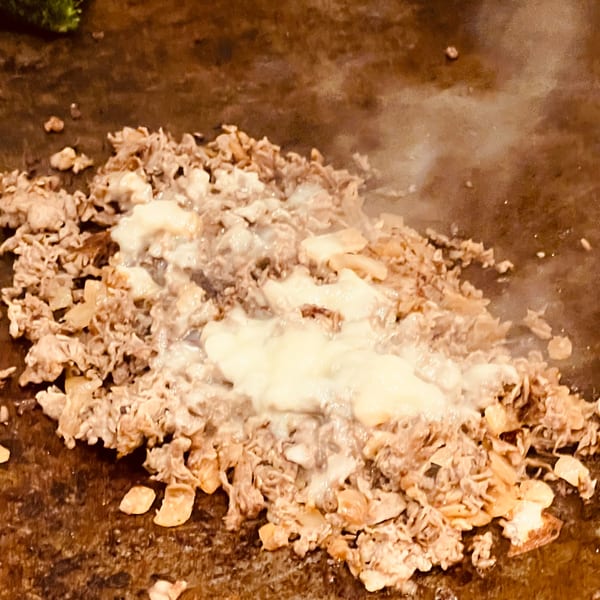 Sizzling Greek gyro meat and melted cheese cooking on a flat-top grill.