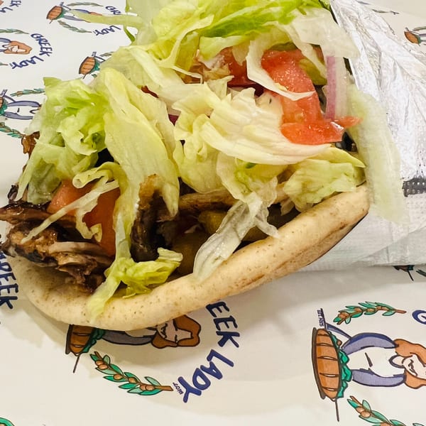 A Greek Lady gyro with meat, lettuce, and tomatoes, partially wrapped in foil.