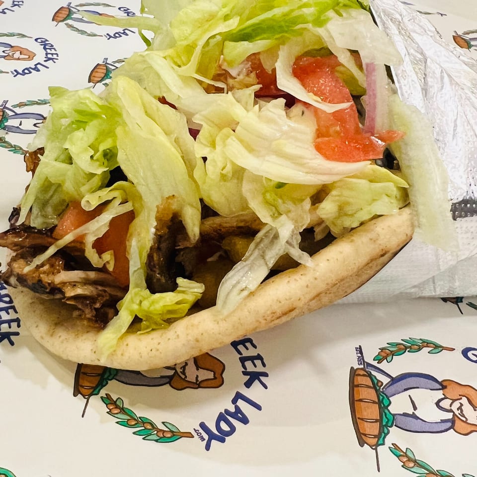 A Greek Lady gyro with meat, lettuce, and tomatoes, partially wrapped in foil.